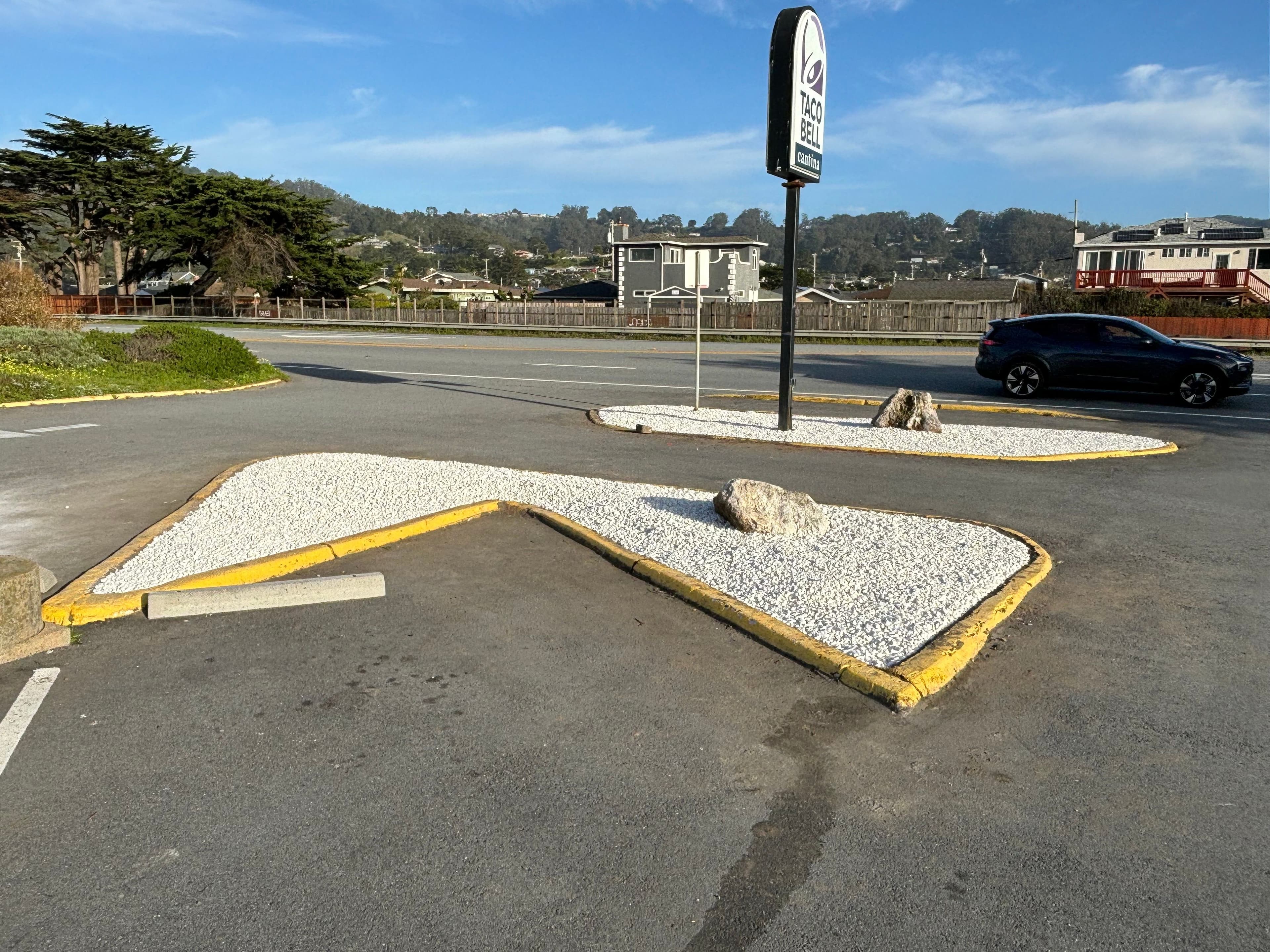 Parking lot with curvy white gravel landscaping and a Taco Bell sign in the background.