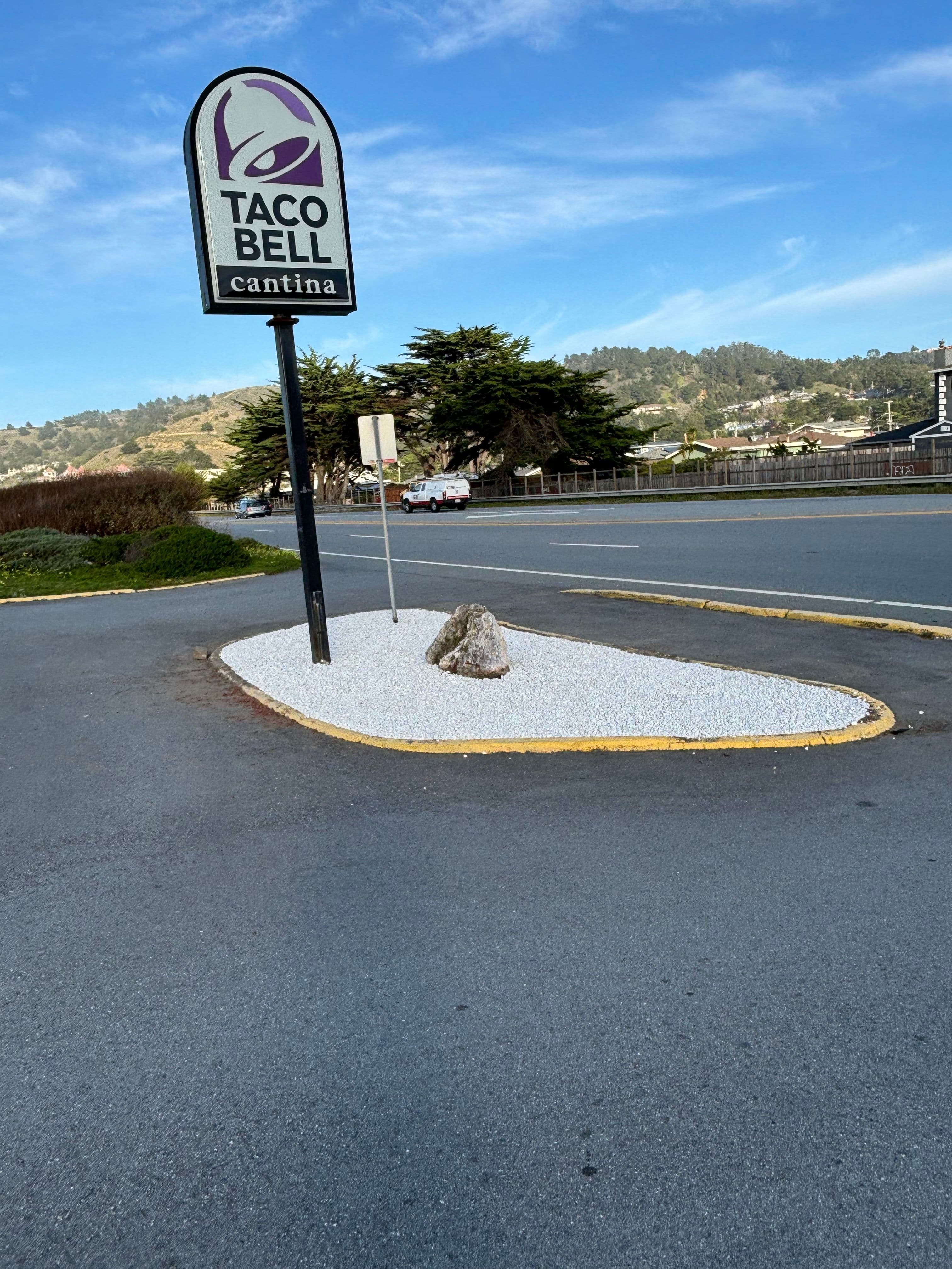 Taco Bell Cantina sign near a gravel landscaping feature on a sunny day.