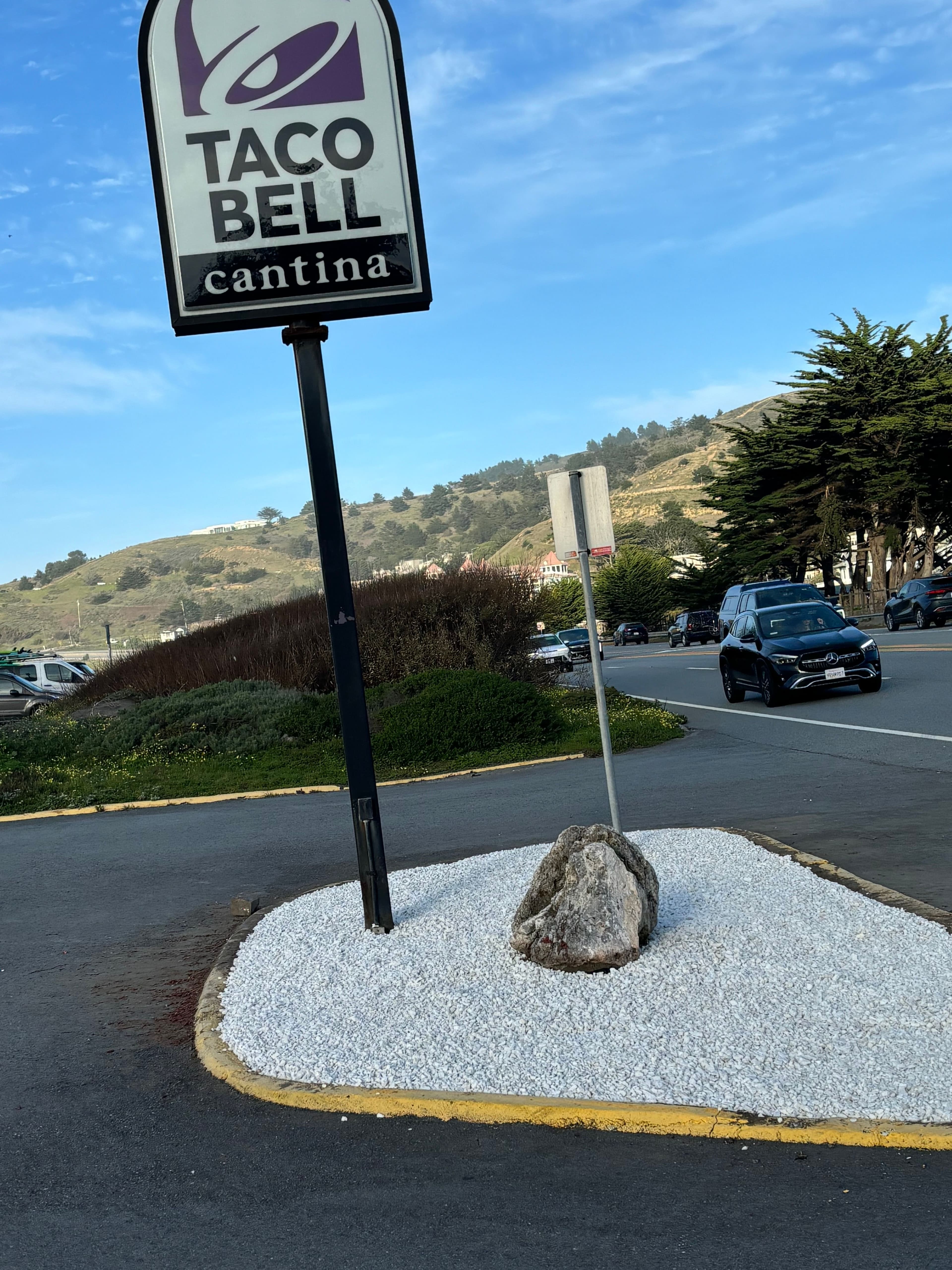 Taco Bell Cantina sign with white gravel and boulder in foreground on a sunny day.