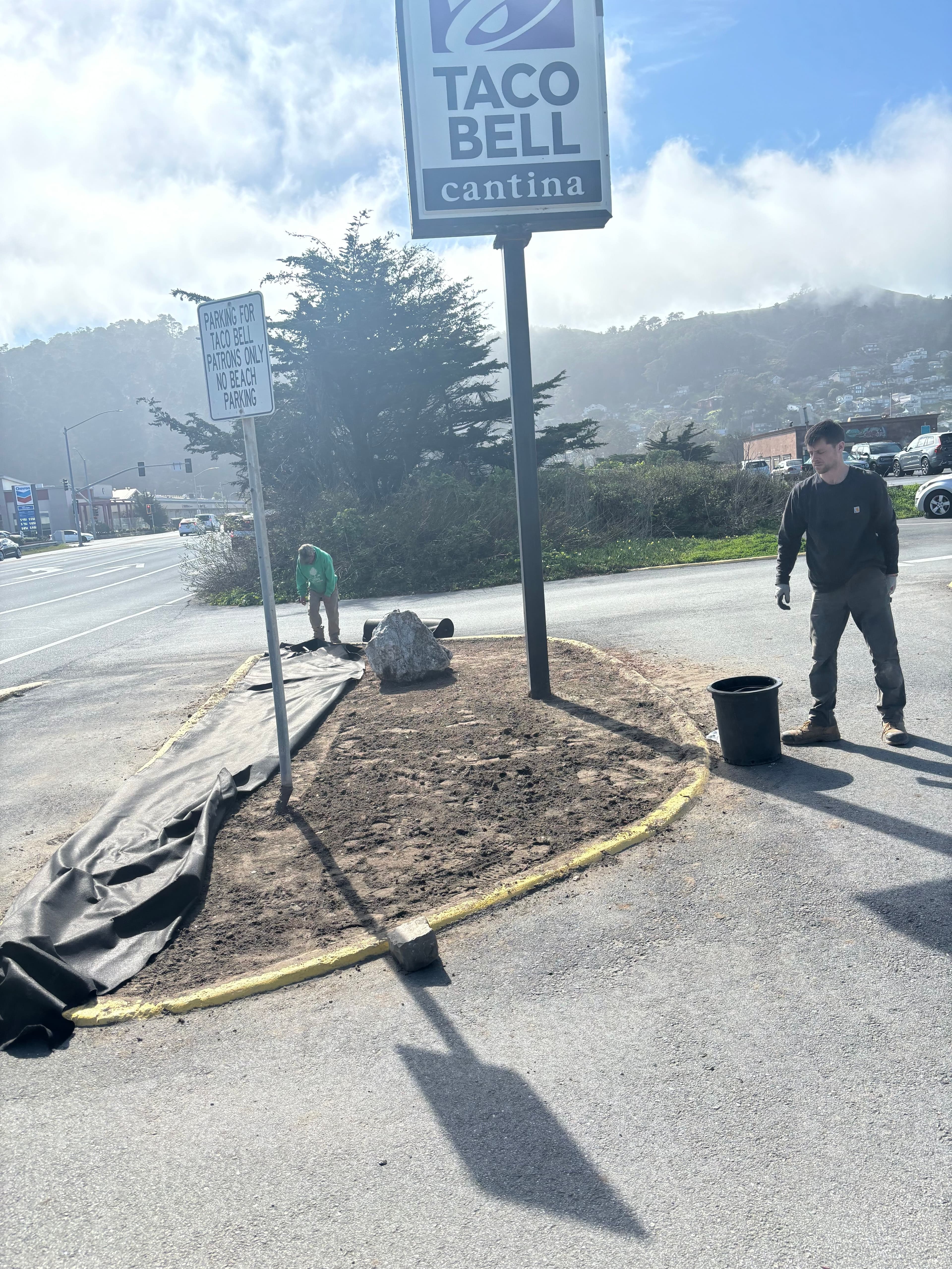 Taco Bell sign with workers preparing landscaping near the cantina location.