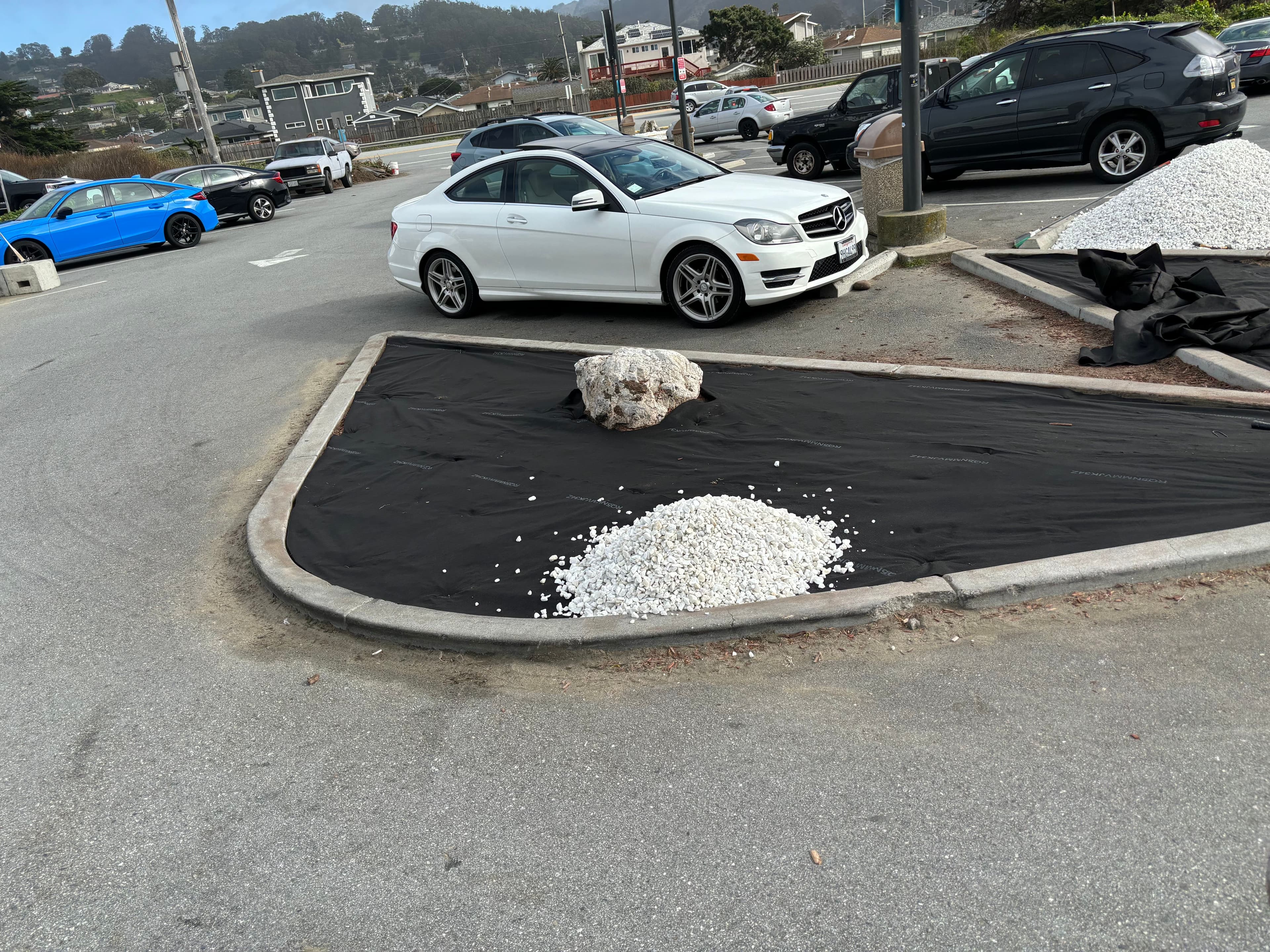 White car parked near gravel and a rock on a black tarp in a lot.