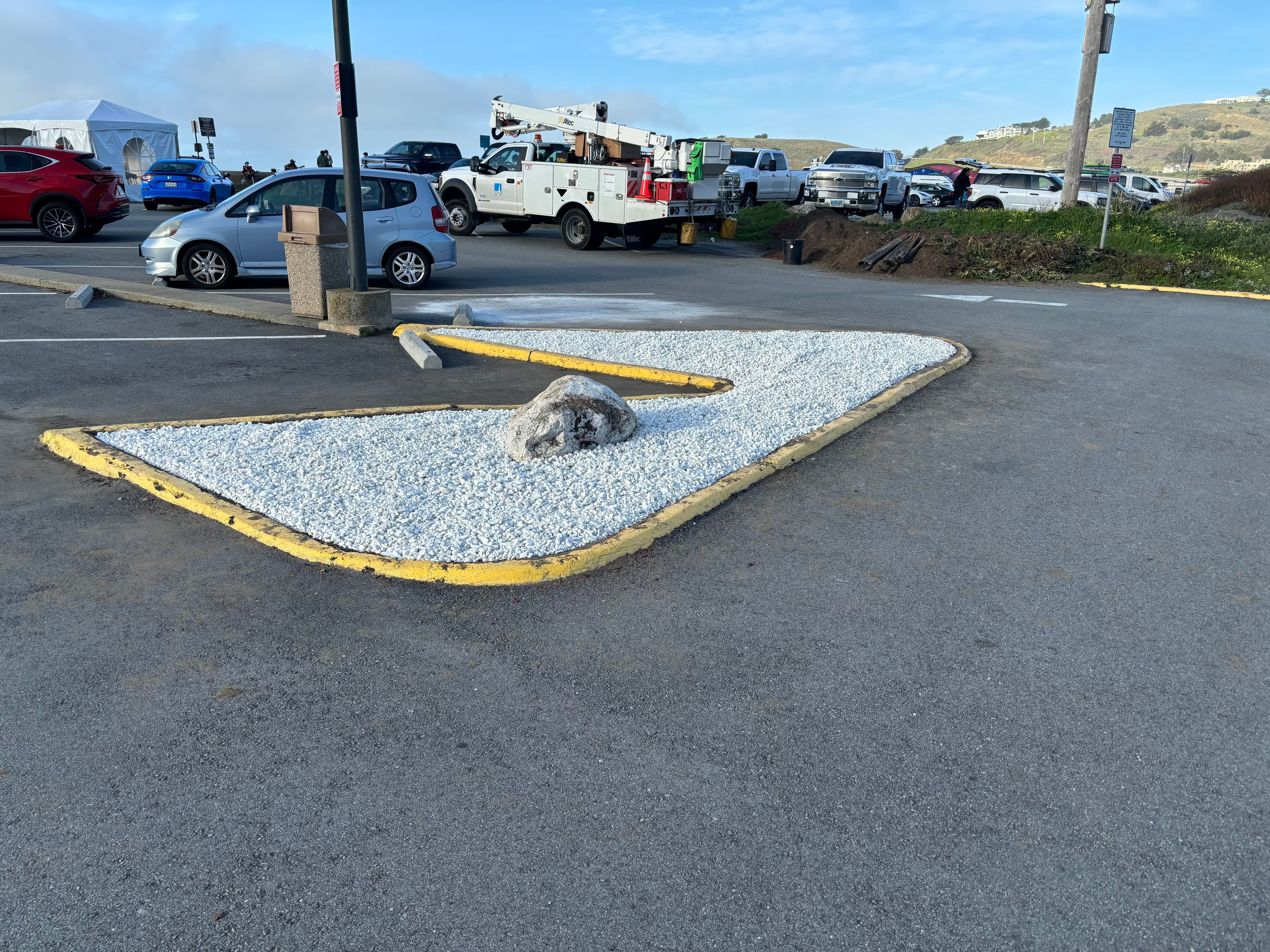 Parking lot with a gravel landscape feature and a large rock, surrounded by asphalt.