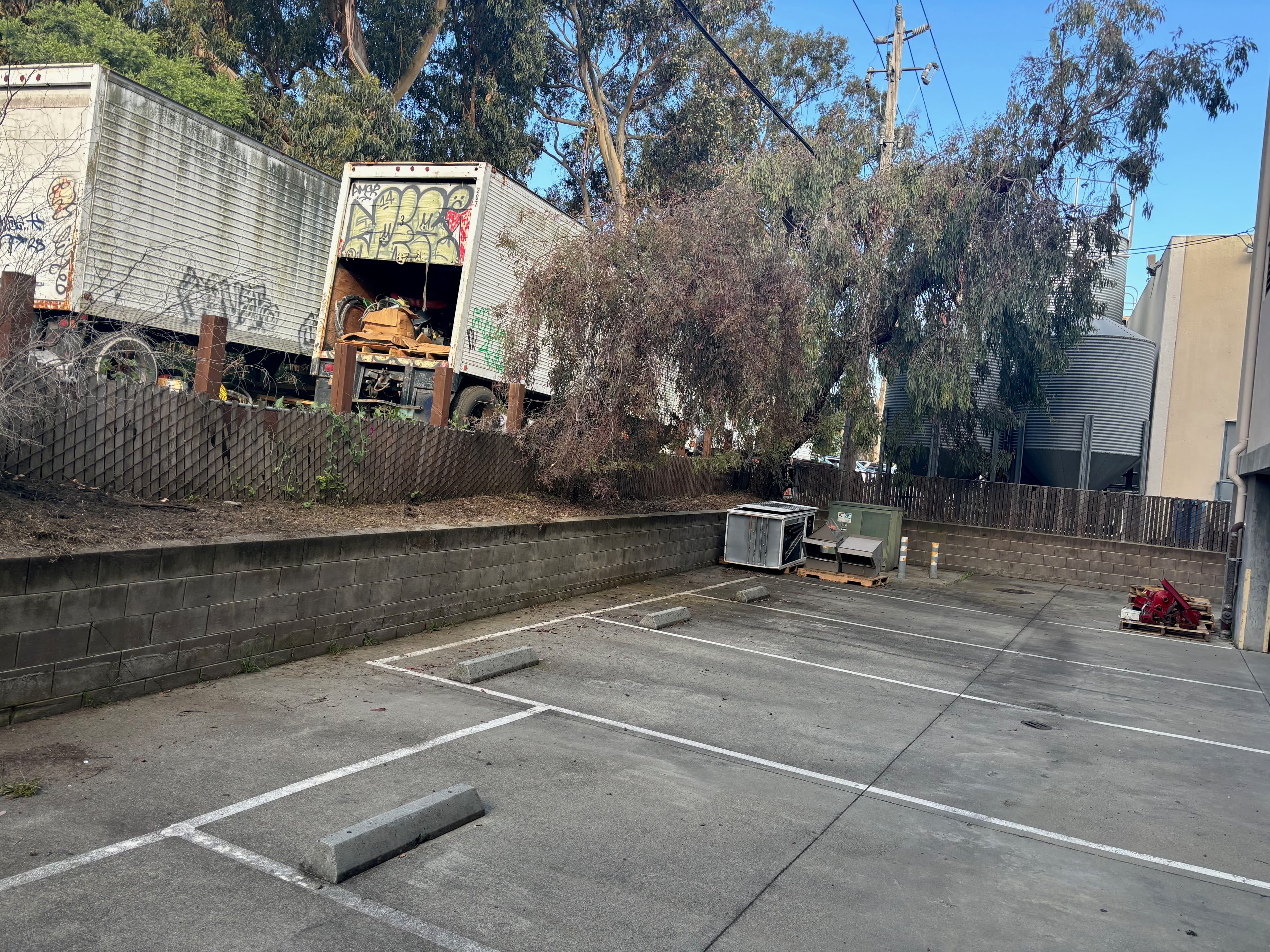 Empty parking lot with graffiti-covered trucks and trees in the background.