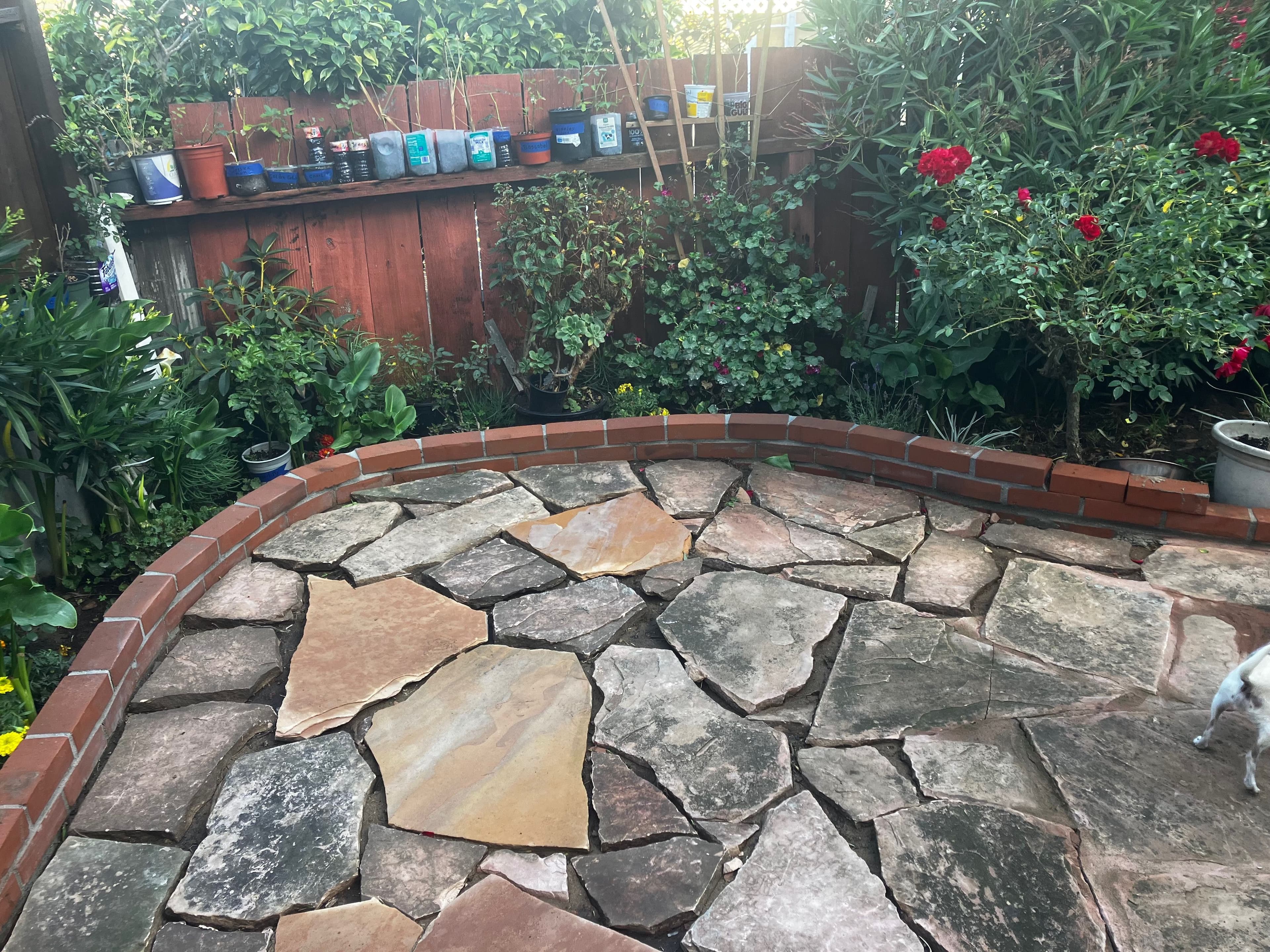 Natural stone patio surrounded by lush greenery and colorful potted plants in a garden setting.