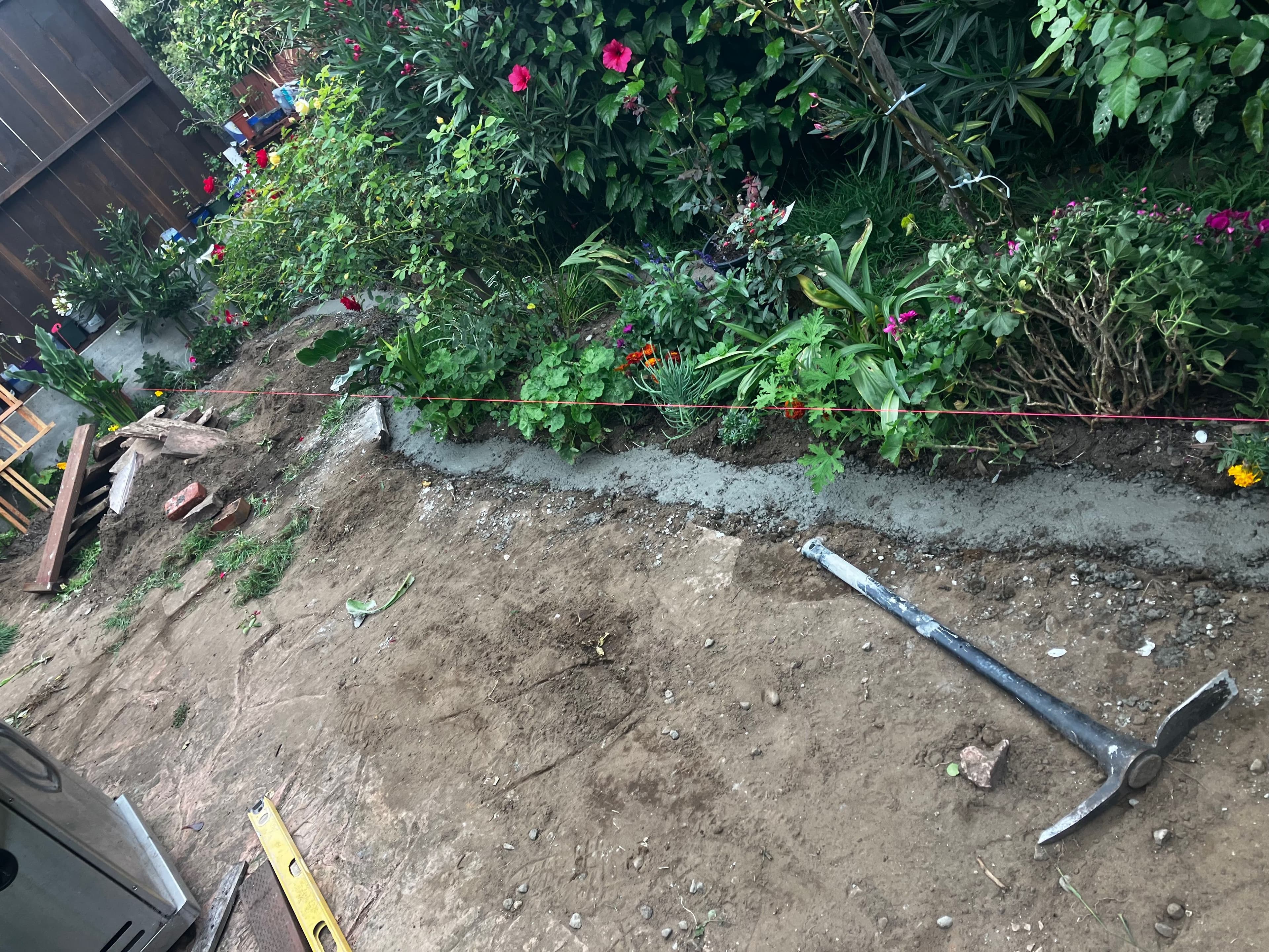Garden landscaping project with freshly poured concrete, tools, and blooming flowers.