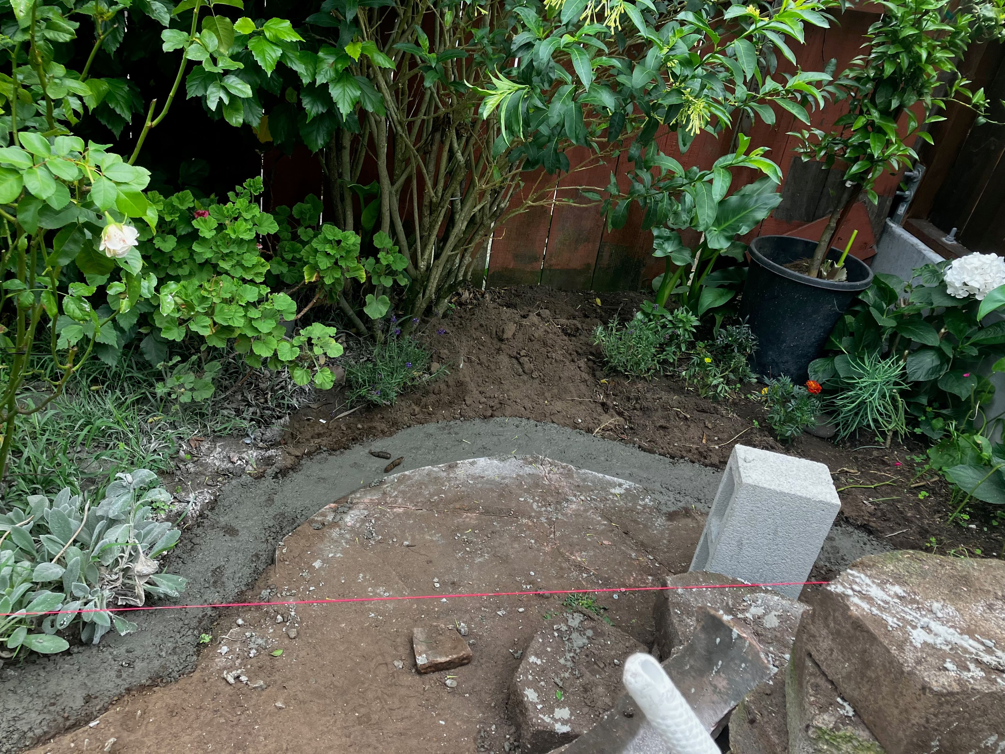 Freshly poured concrete in a garden setting, surrounded by plants and flowers.