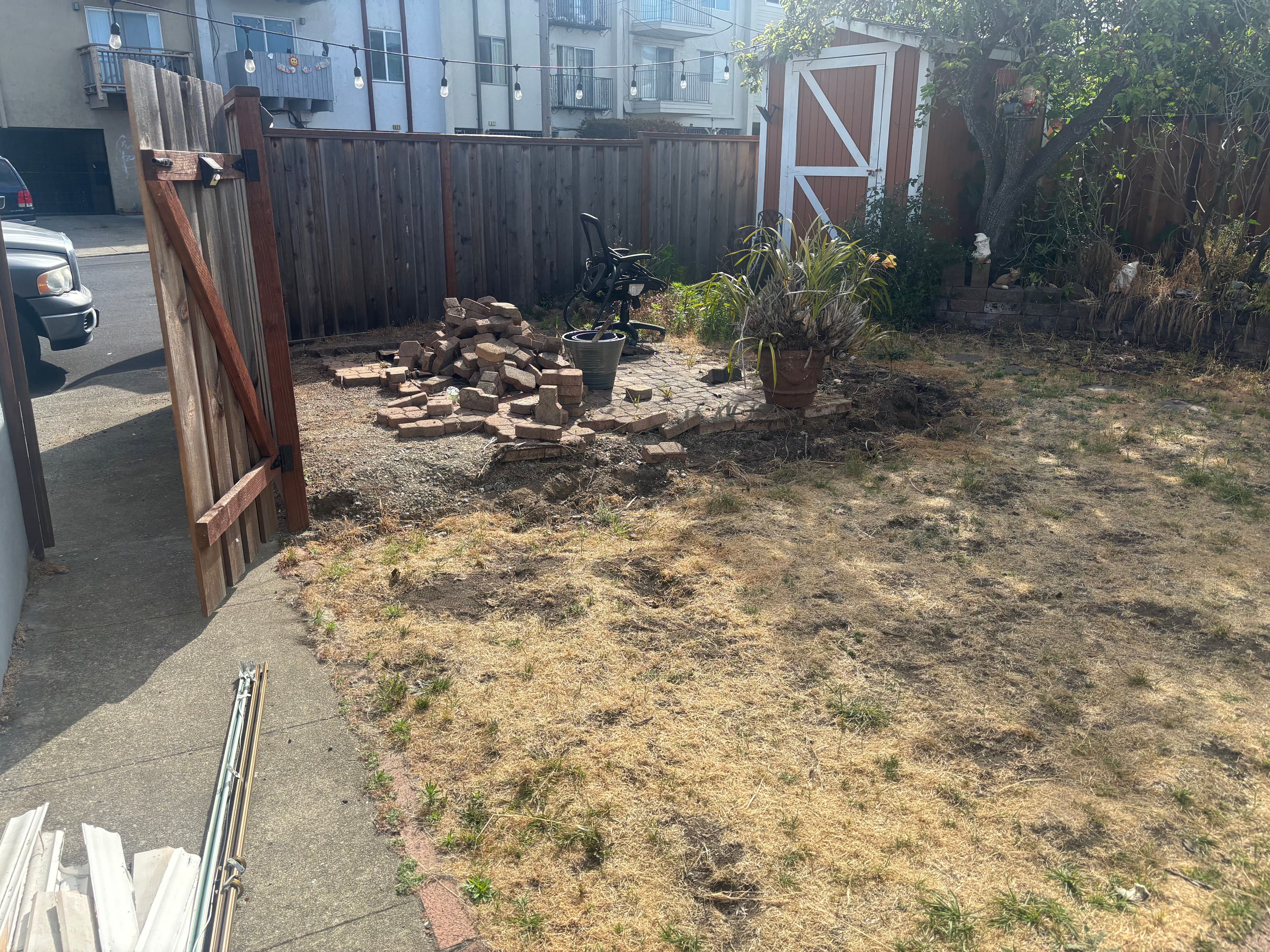 Dry backyard with a wooden gate, brick pile, and outdoor shed surrounded by a fence.