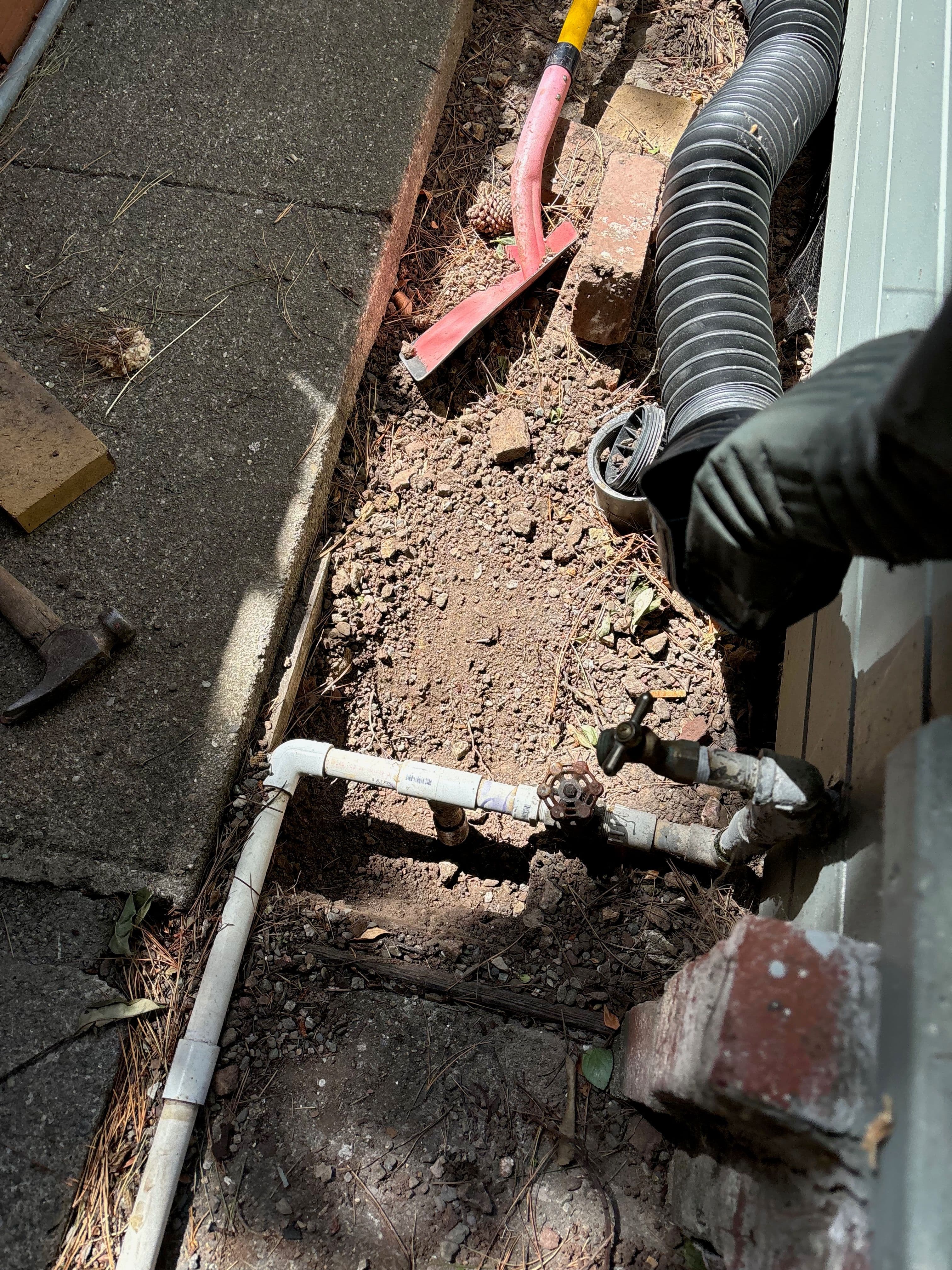 Plumbing maintenance area with pipes, dirt, and tools for repairs.