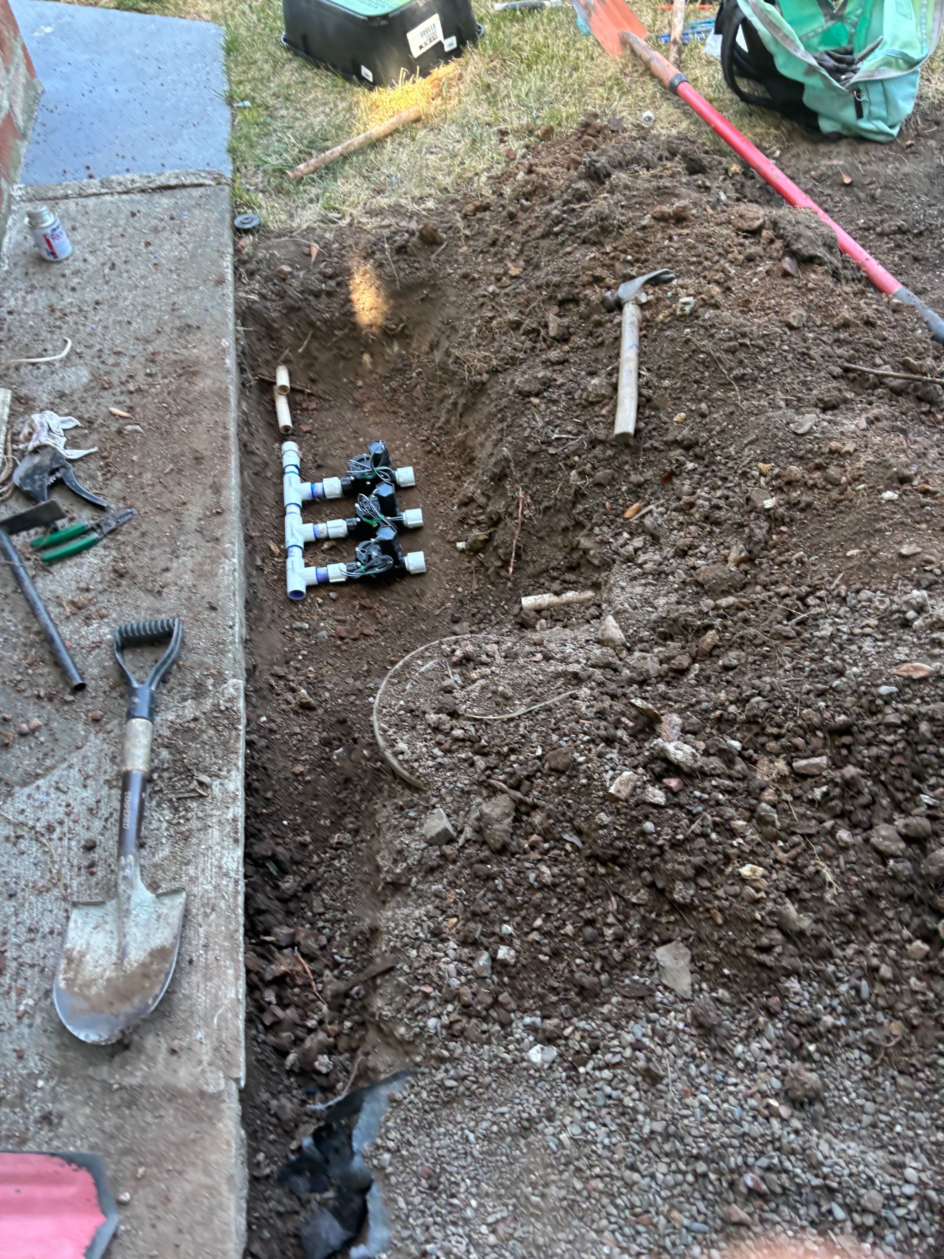 Excavated trench with PVC pipes and gardening tools for landscaping project.