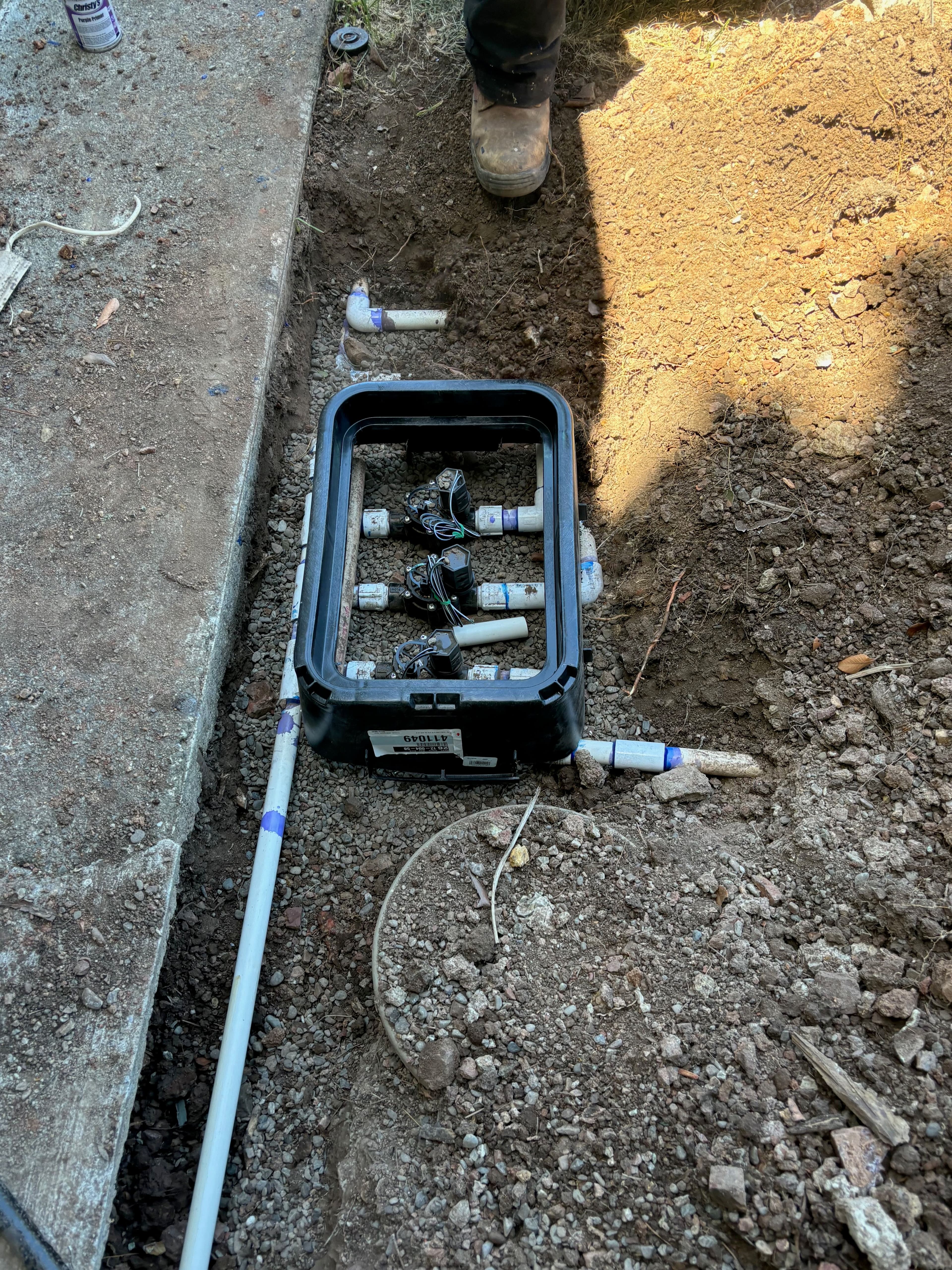 Installation of plumbing pipes in a trench with connectors visible, surrounded by dirt.