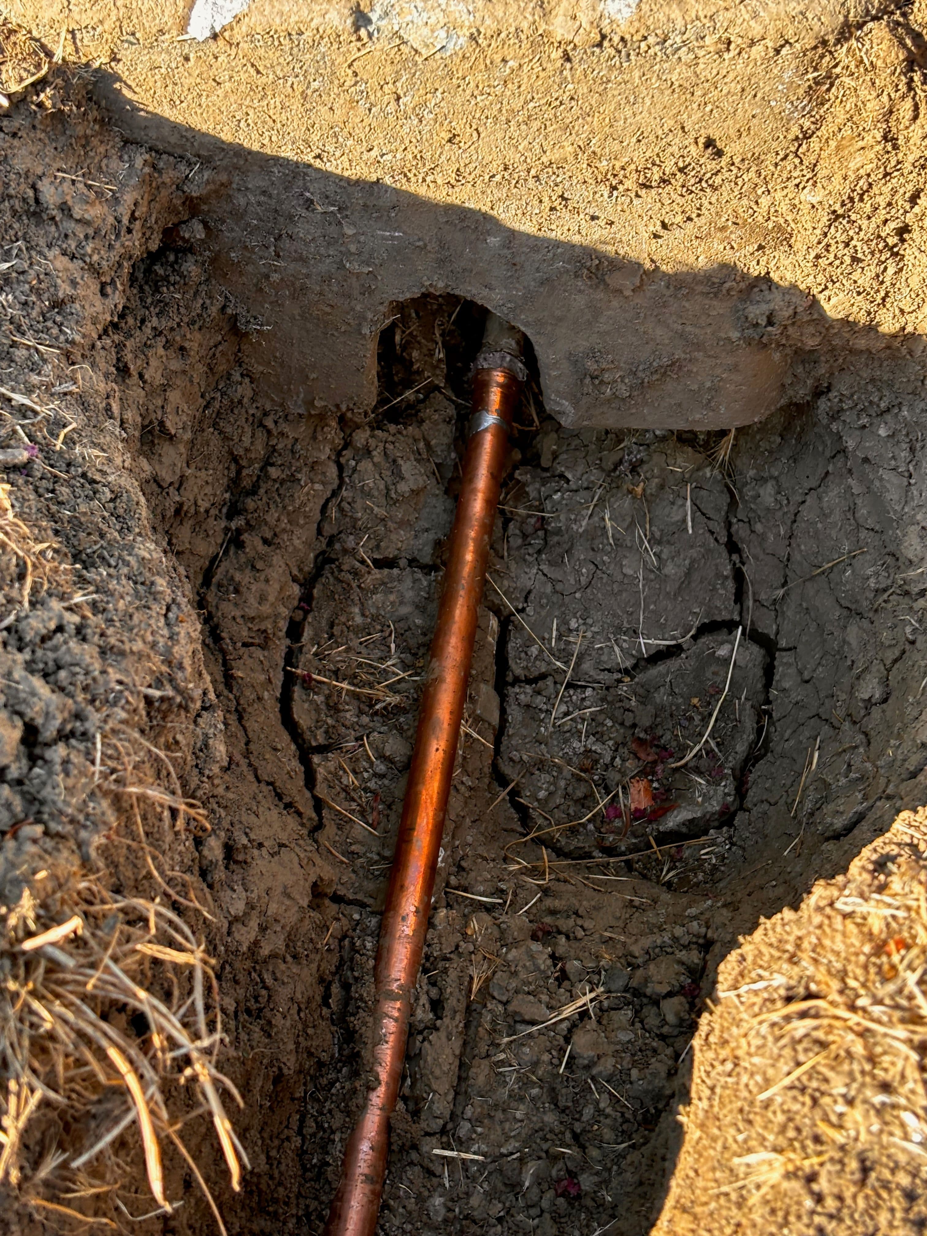 Copper pipe embedded in dry, cracked soil, showing excavation for plumbing repair.