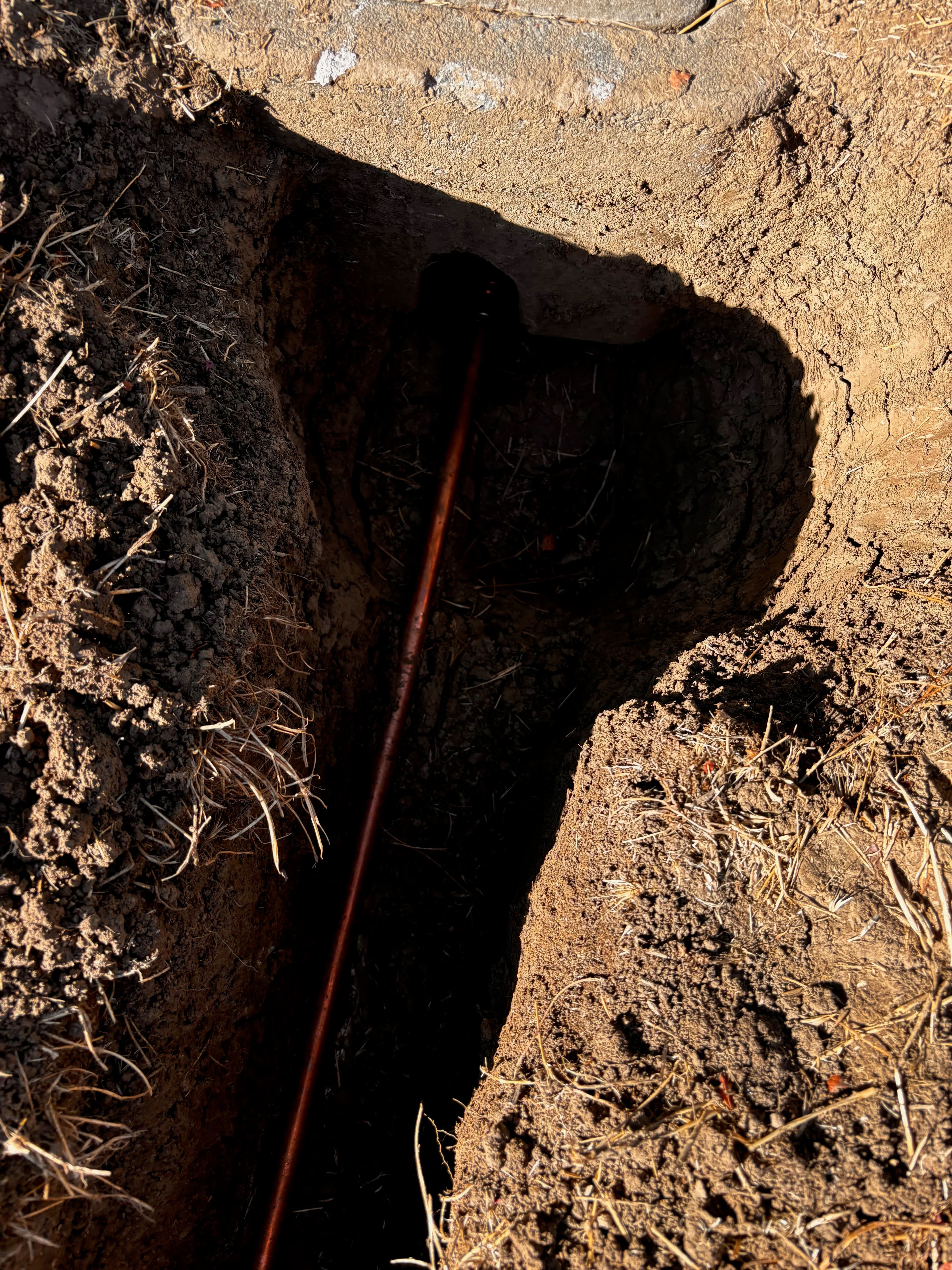 Copper pipe installation trench with dark soil and grass edges.