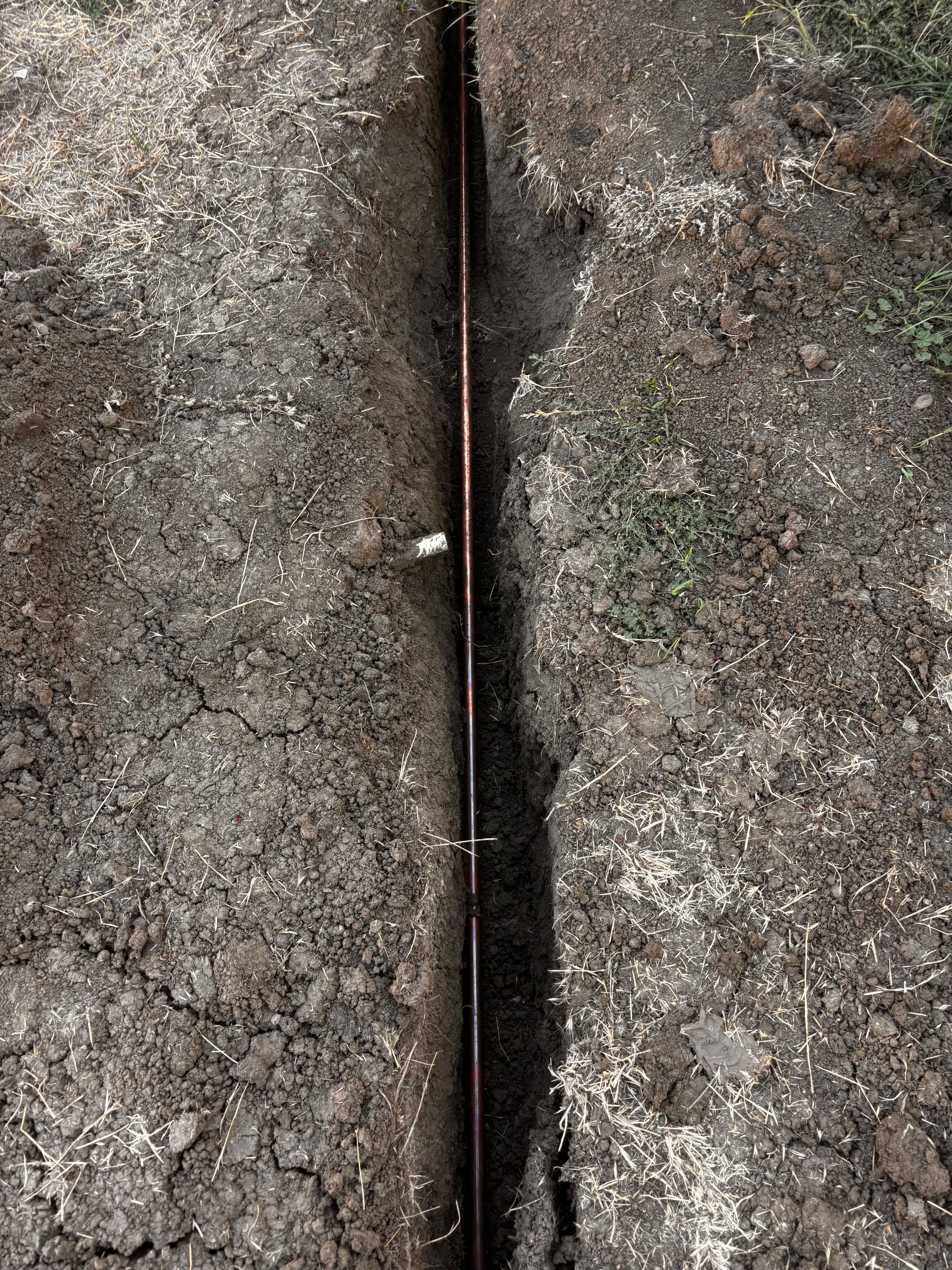Trench showing utility line installation in dry, cracked soil.