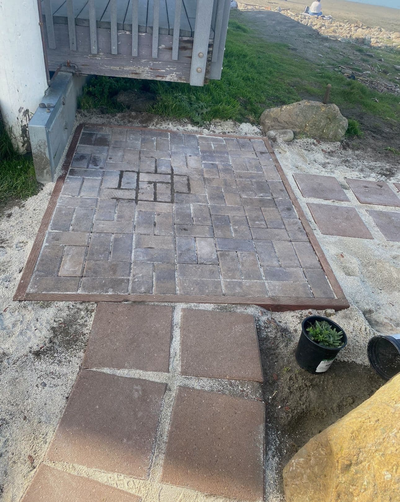 Paved walkway with gray stones leading to a grassy area by the seaside.