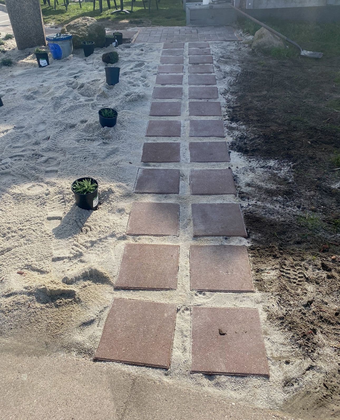 Pathway made of stone pavers surrounded by sand and potted plants in a garden setting.