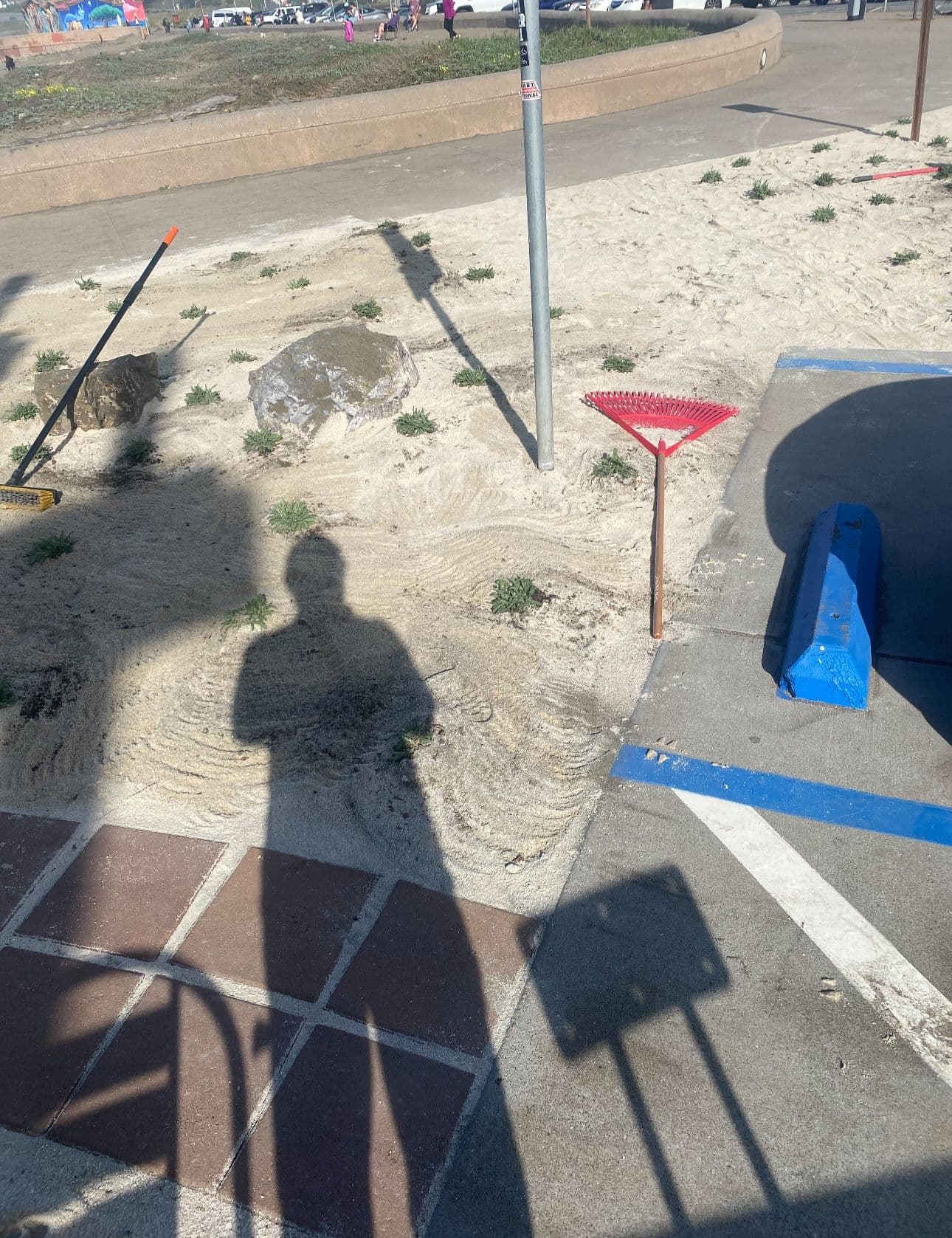 Beach pathway with sandy surface, rocks, and shadows of people and equipment.