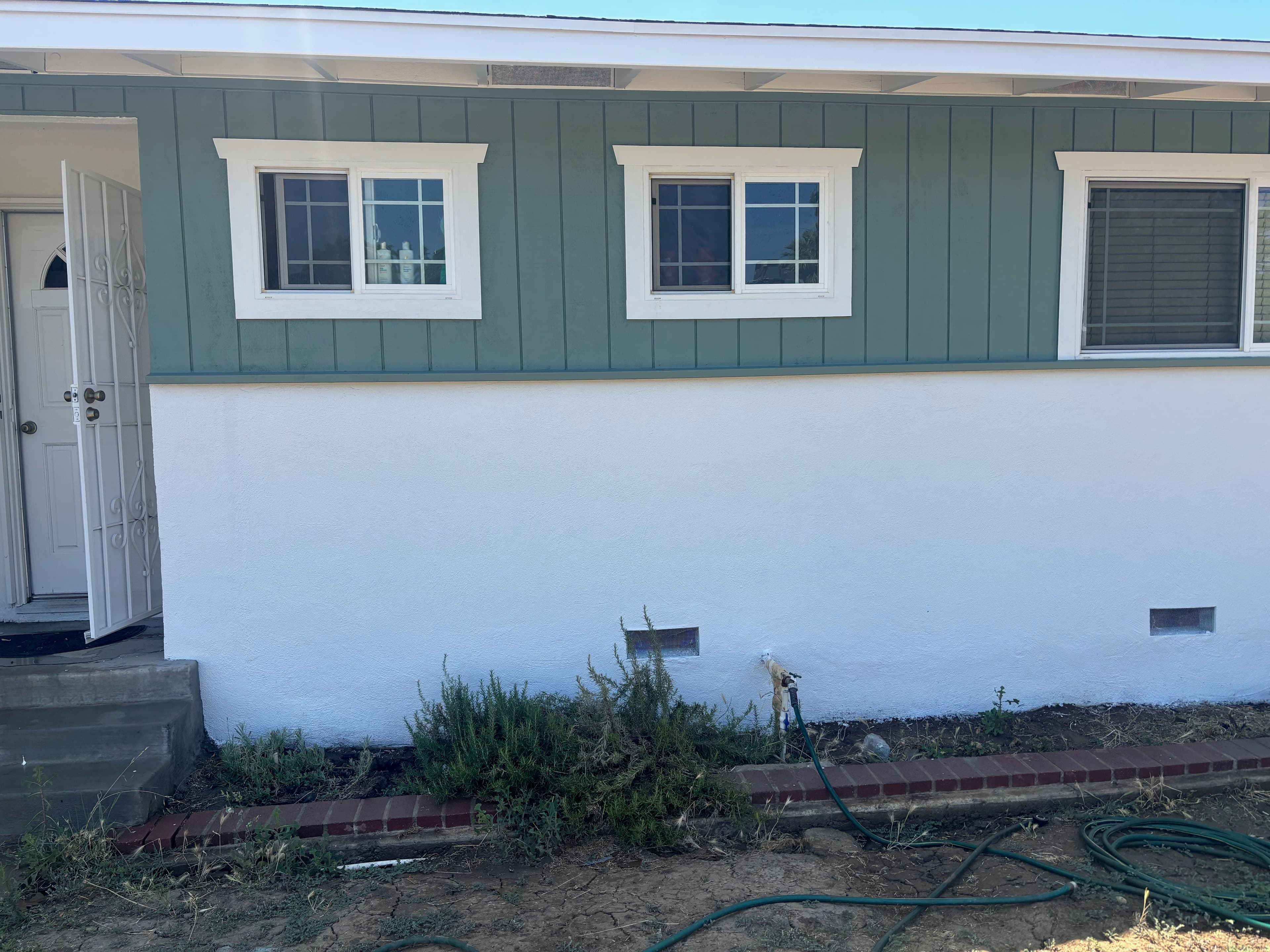 Exterior view of a house showing green siding, white trim, and a well-maintained entrance.