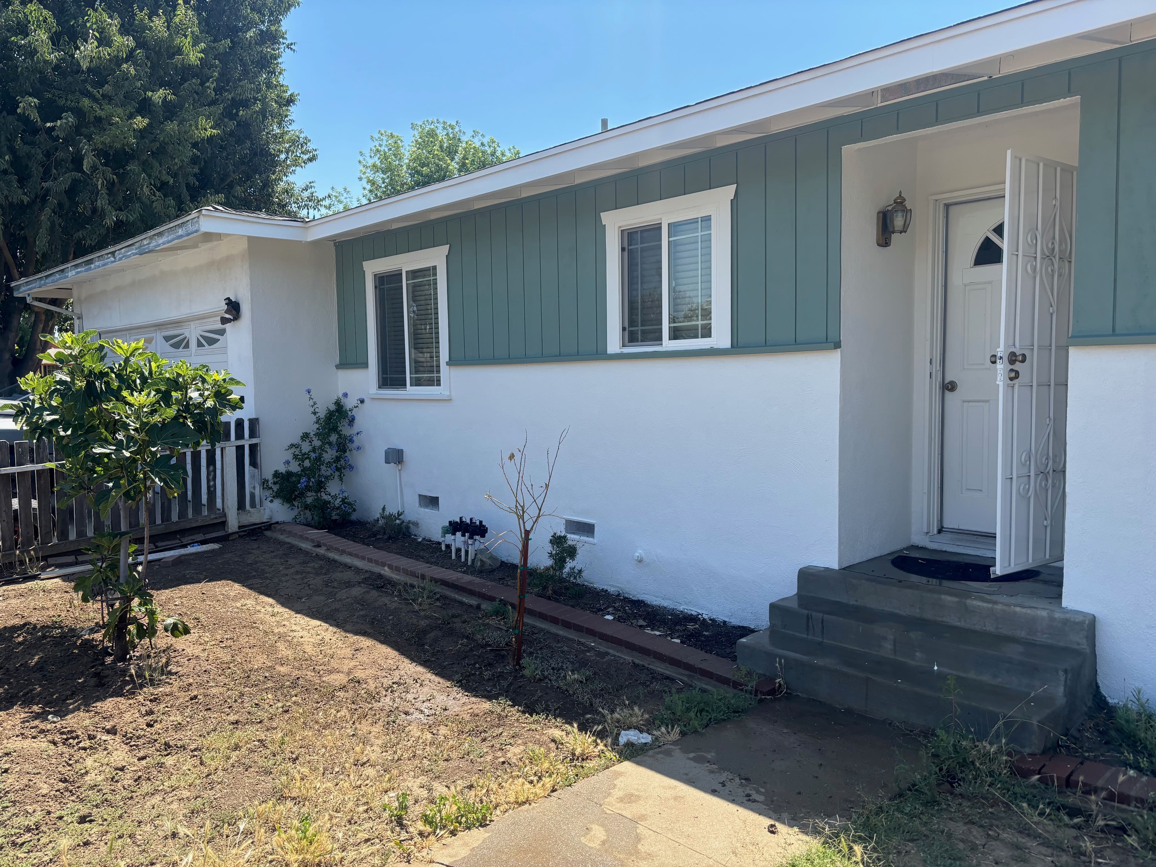 White exterior home with teal accents, front steps, and small garden area. Bright sunny day.
