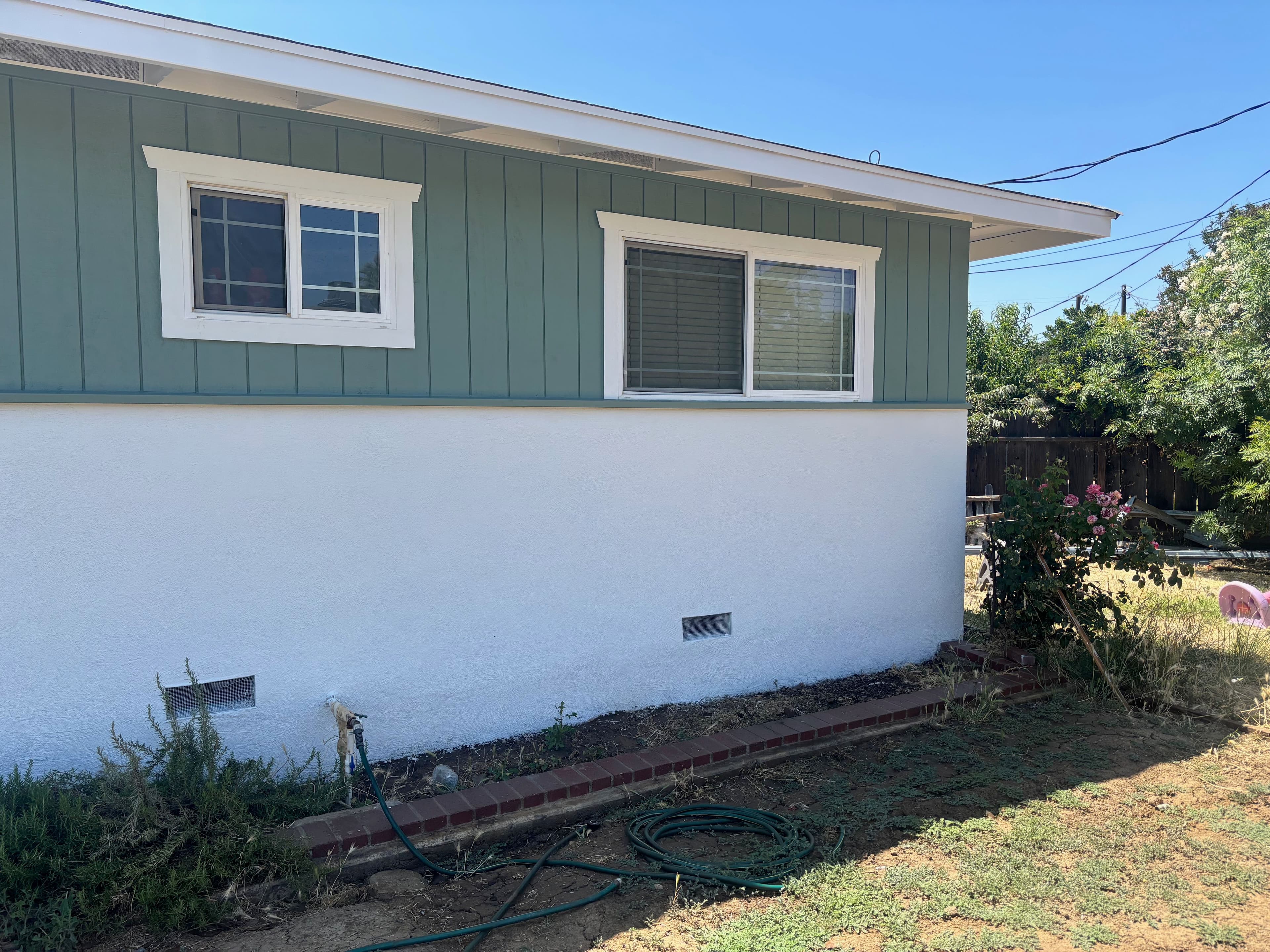 Side view of a house with blue-green siding, white walls, and landscaping in the yard.