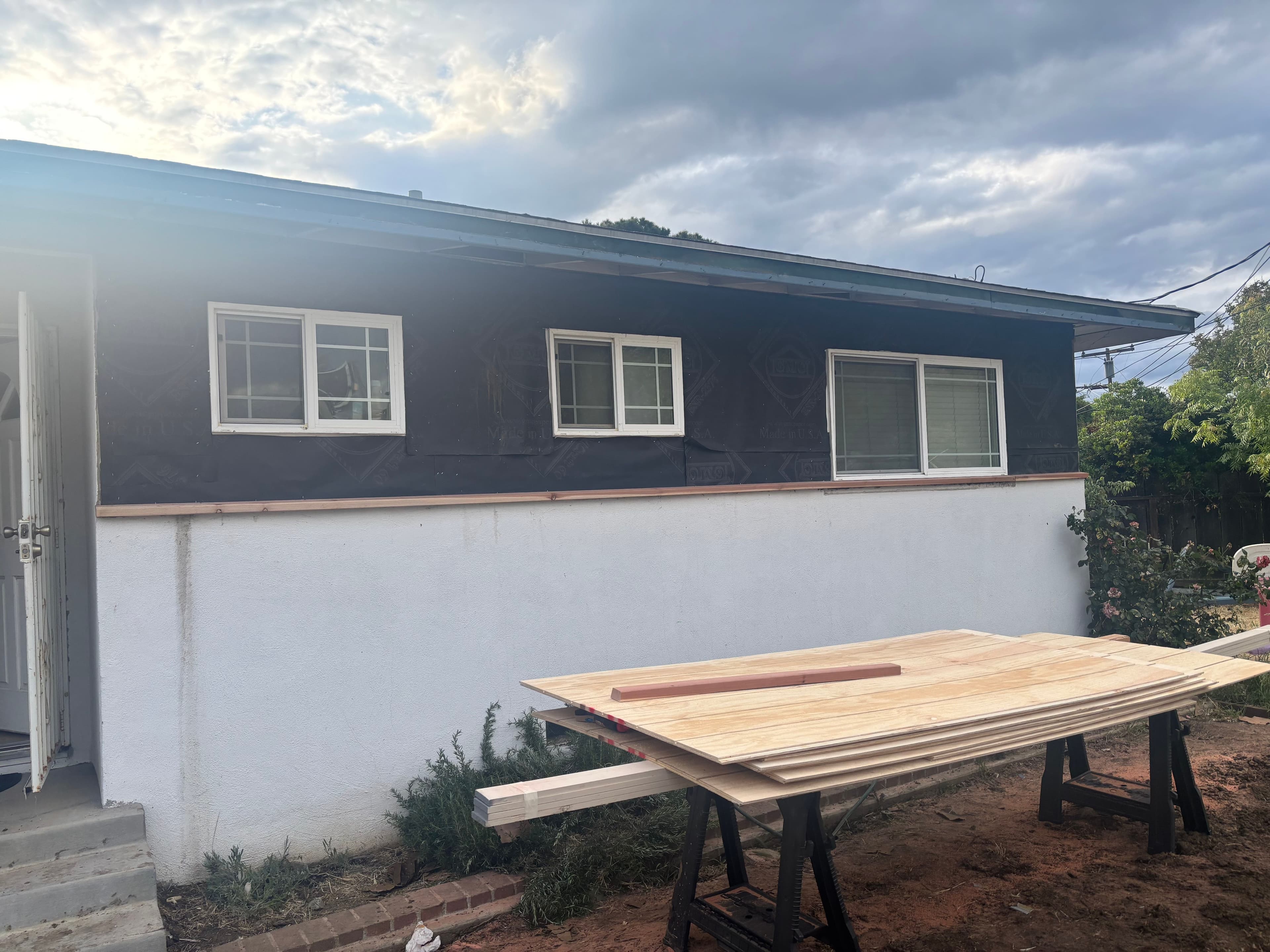 Exterior view of a house under renovation with wooden boards on a table in front.