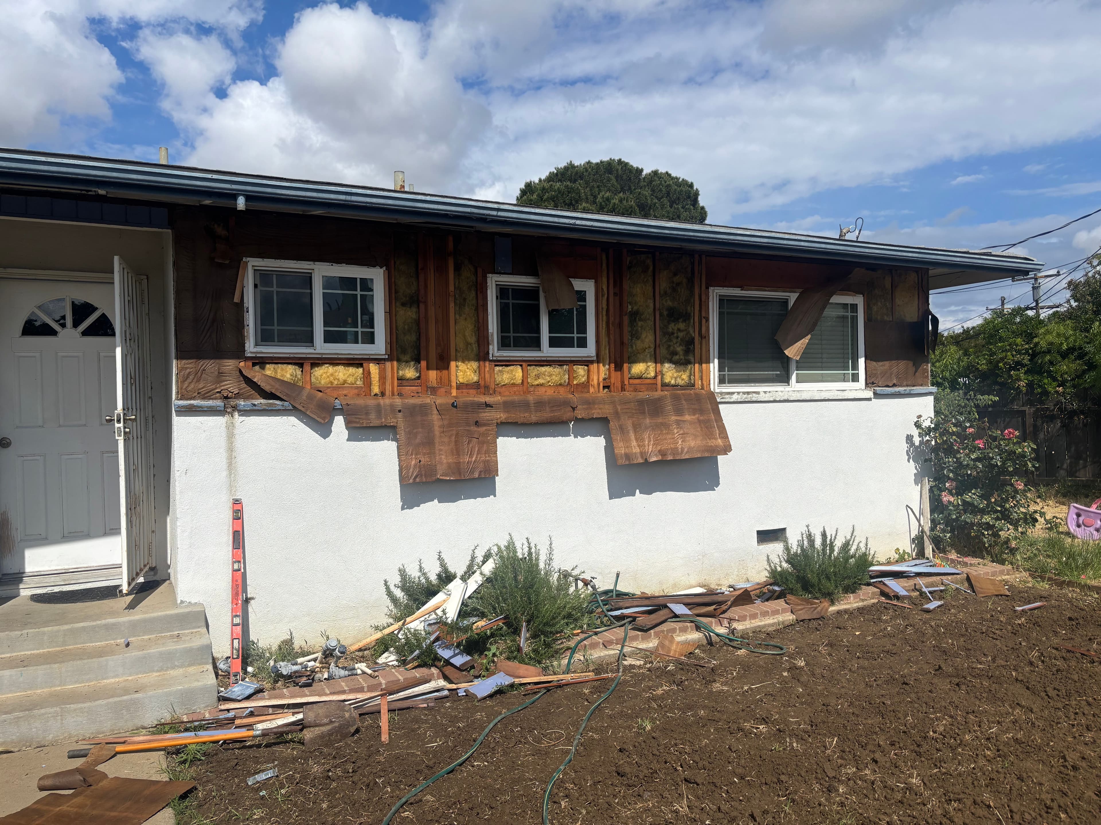 Home exterior renovation with exposed wood, construction debris, and cloudy sky.